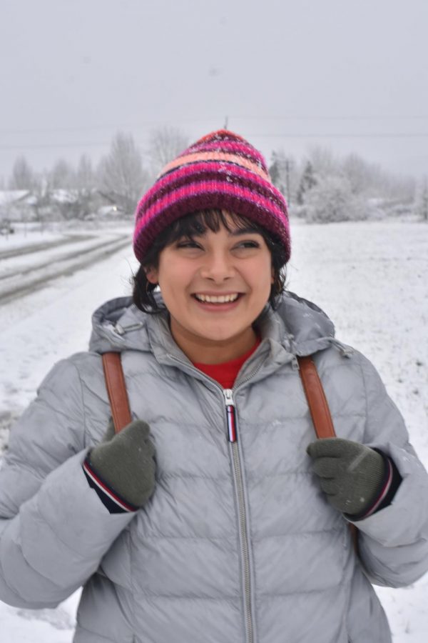 Denisse Baltazar local Corvallis resident taking a walk in the snow. Holding her backpack as she smiles into the snowy distance.