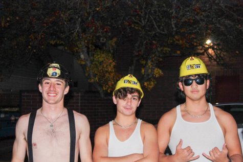 Three students dressed as a firefighter and construction workers pose for a picture at night.