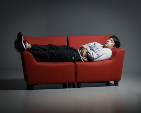 I person takes a nap on a couch in a dark, empty room.