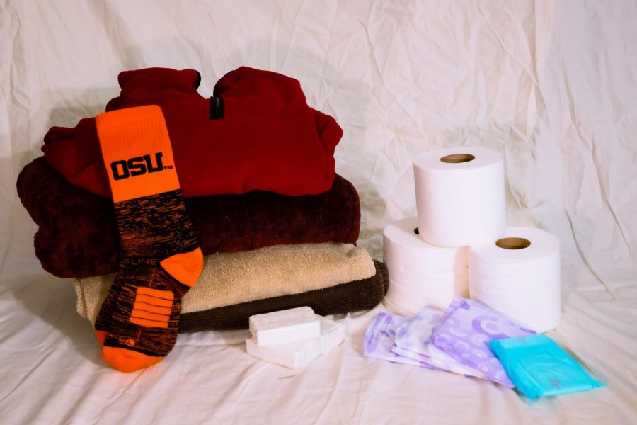 A pile on warm winter clothing sits next to other donation items like socks, feminine hygiene products, bars of soap and several rolls of toilet paper.