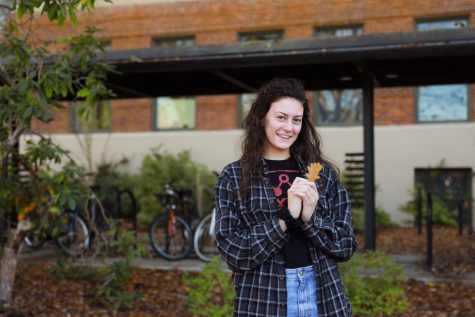 Katie Papineau smiles with a brown leaf on the OSU Corvallis campus.