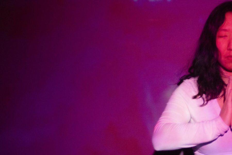 Julianna Souther meditates, but the photo is cropped where only Southers right side is showing. A projector is projecting a pink light across Souther and the background.