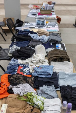 A table covered in clothing items ranging from t-shirts and jeans to sweatpants, tank tops and lingerie.