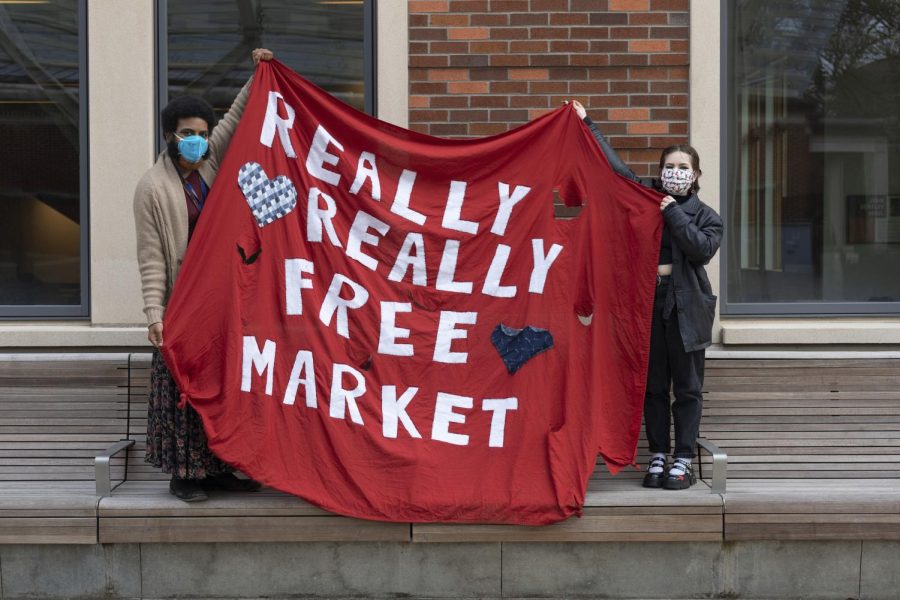 Julian Clarke, left, and Lena Randall stand on a bench and hold up a homemade fabric banner that reads Really Really Free Market with hearts around it.