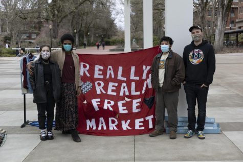 From left to right: Lena Randall, Julian Clarke, Johnny, and Nik Price hold up a homemade fabric banner that reads "Really Really Free Market" with hearts around it.