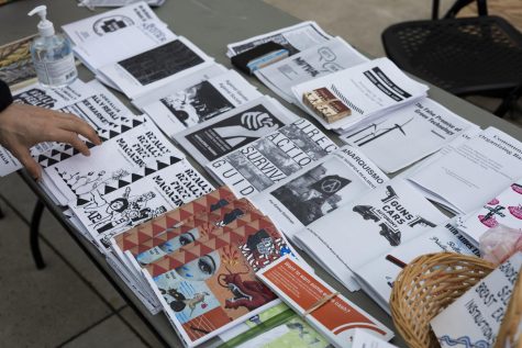 A hand reaches for one of the many zines neatly lined up on a table.