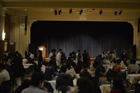 A large crowd mingle amongst themselves as they sit around tables.