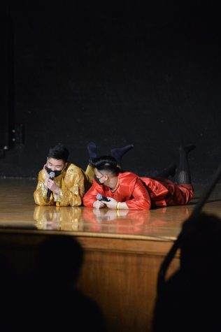 Aaren Kong, left, and Austin Peng lay on their stomachs on stage while Kong speaks into the microphone.