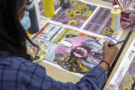 Leah Venkatesan paints a record—the photo is taken from over her should, looking down at her art. Her art features a large abstract face.