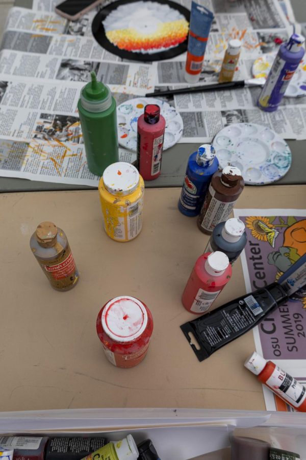 Bottles of paint sit on the newspaper-covered tables.