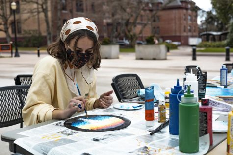 Amelia Noall wears a crewneck sweatshirt with a polka dot scarf in her hair as she paints a record.