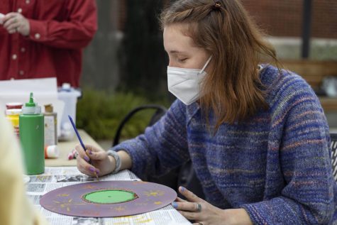 Amanda Appel wears a striped knit sweater as she paints a record.