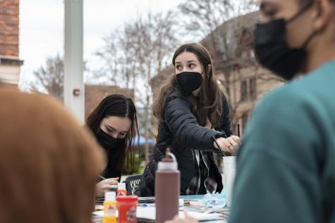 Lily Middleton, left, sits painting as Georgina Paez, wearing a puffer jacket, stands to collect art supplies.