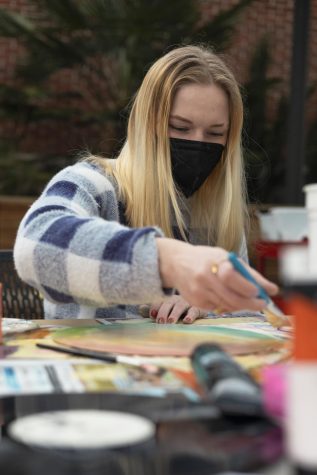 Grace Brod wears a checkered sweater as she paints a record.