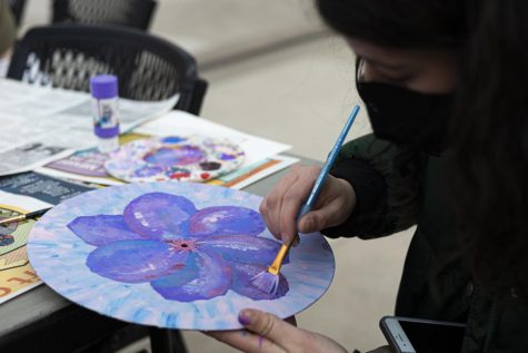 Mylea Braun paints a record—the photo is taken from over her should, looking down at her art. Her art features a large flower in the center of the record.