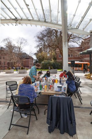 A group of students and KBVRfm organizers mingling around the table with a Beaver Bus in the background.