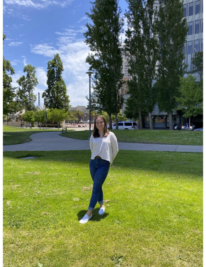 Taylor Bacon poses for a photo outside in a patch of grass in front of a large building