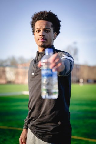 Dante Williams holds a plastic, single-use water bottle out towards the camera while wearing an OSU Beavers shirt.