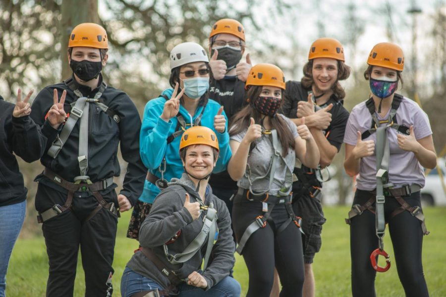 A group of people wear harnesses and helmets while smiling and giving a thumbs-up.