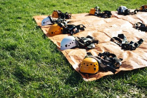 Harnesses and helmets are laid out on a tarp in the grass.