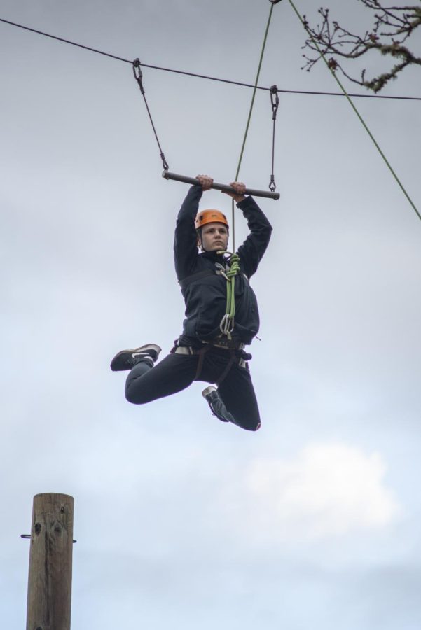A student jumps from a post to a swinging bar as they make their way through the challenge course in the air.