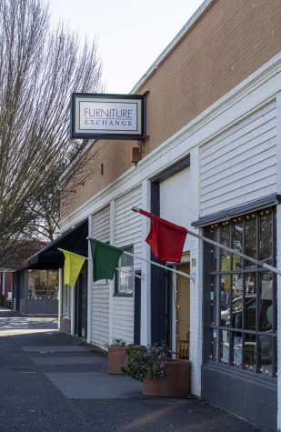 The Furniture Exchange sign hangs above its door with colorful flags along the storefront.