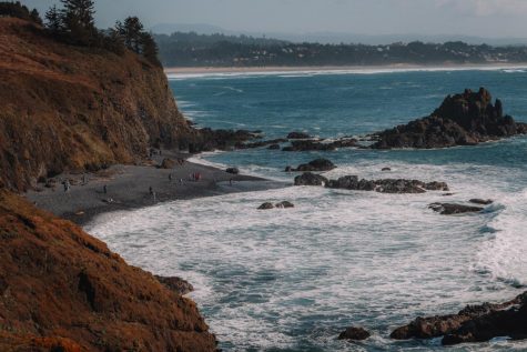 A view of an Oregon Coast beach with a crown of people on the sand down below.