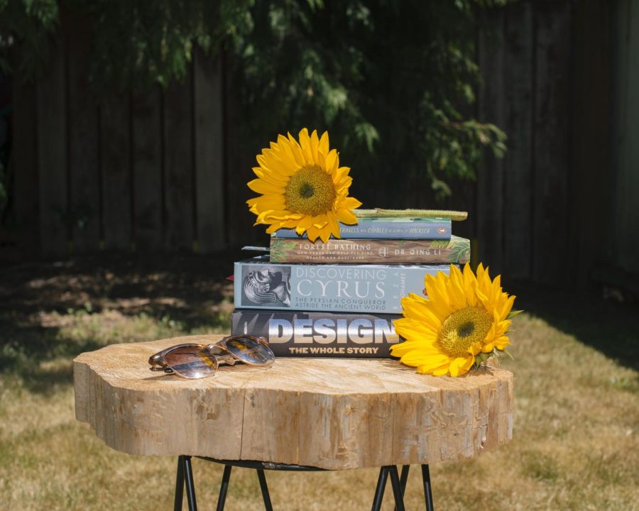 A photo illustration of a stack of books and sunflowers signifying reading for class and for fun in the summer months in Corvallis Ore. on July 20, 2022. Librarians and professors recommended several books for community members to read this summer.