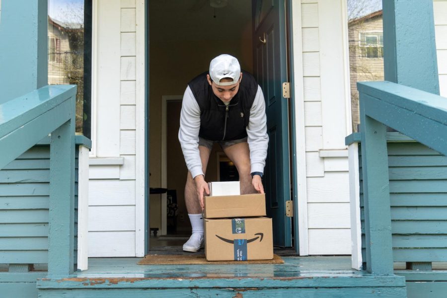 A photo illustration of third year, Lucas Fischer (he/him), picking up boxes on his porch on April 24 in Corvallis. Many websites and companies offer discounts to students enrolled in classes.