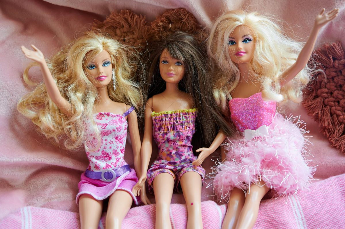 Barbie dolls wave and sit together against a pink backdrop on Aug. 7.