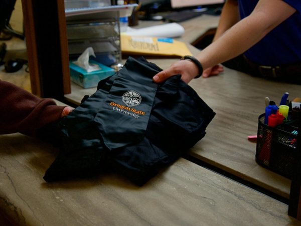 Staff at the Oregon State University Memorial Union desk pass student graduation gowns as a part of the Grads Give Back gown recycling program.